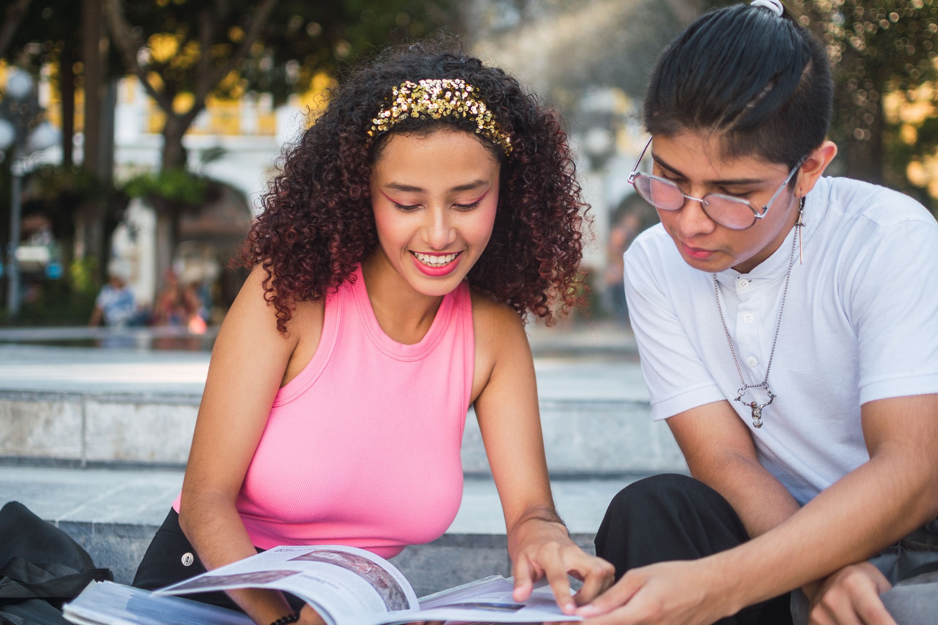 Two young adults reading a magazine in a city park